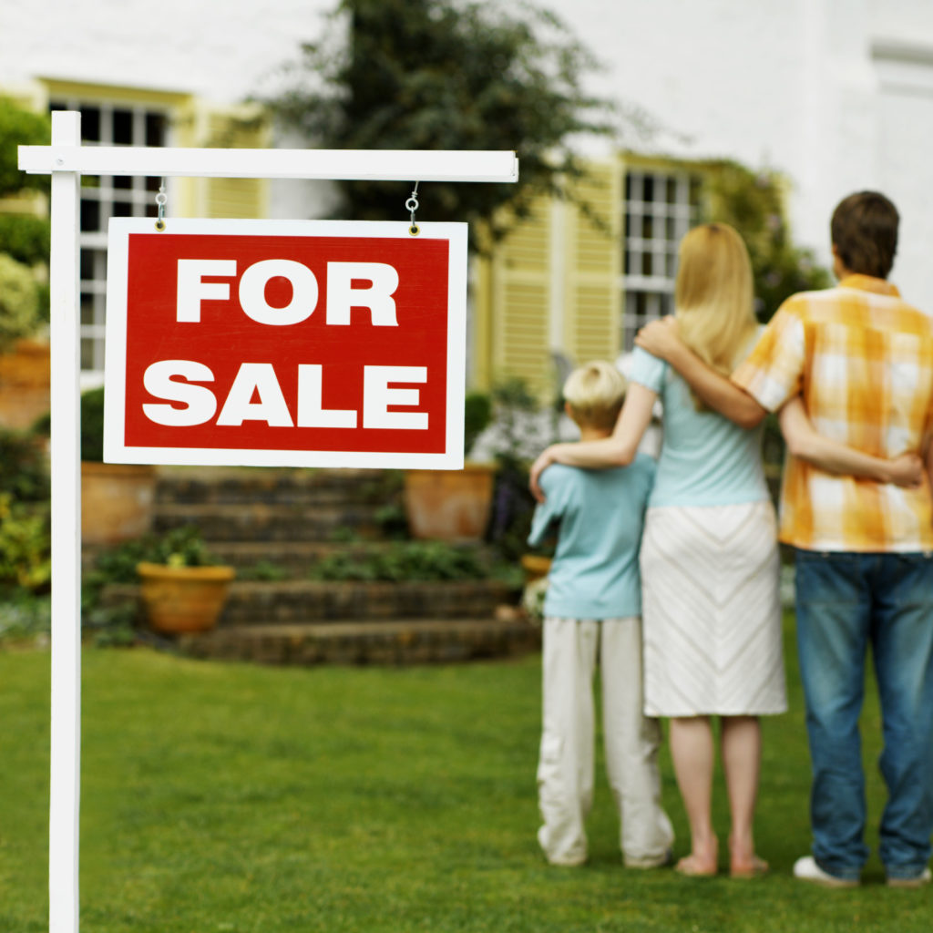 Family standing outside of house with a for sale sign wanting to sell their house fast